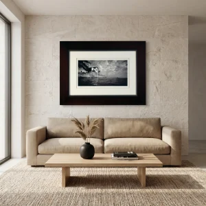 Beige sofa in a modern living room with a low wooden coffee table, a black vase of dried grasses, and a large framed black-and-white photograph on a stone wall.