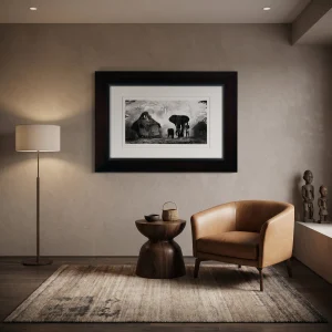 Modern living room corner with a tan leather armchair, round dark wood side table, floor lamp, and a large framed black‑and‑white photo of huts and elephants above the wall.