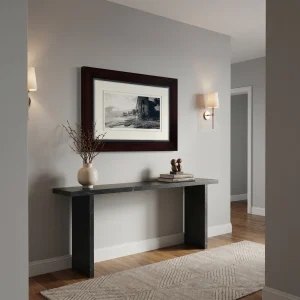 A minimalist entryway with a dark stone console table, framed black-and-white coastal photograph, and a vase with dried branches against a gray wall