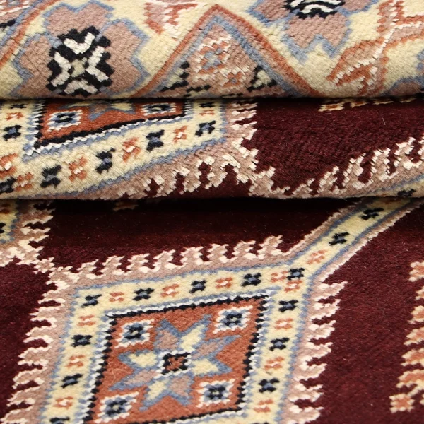 Close-up of stacked oriental rugs with geometric medallions in red, beige, blue.
