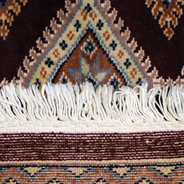 Close-up of a decorative woven rug with fringe along the edge and a geometric diamond pattern in brown, cream, and blue.