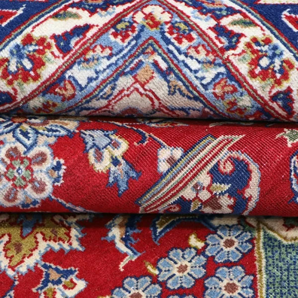 Stack of colorful Persian-style rugs with red, blue, and floral patterns.
