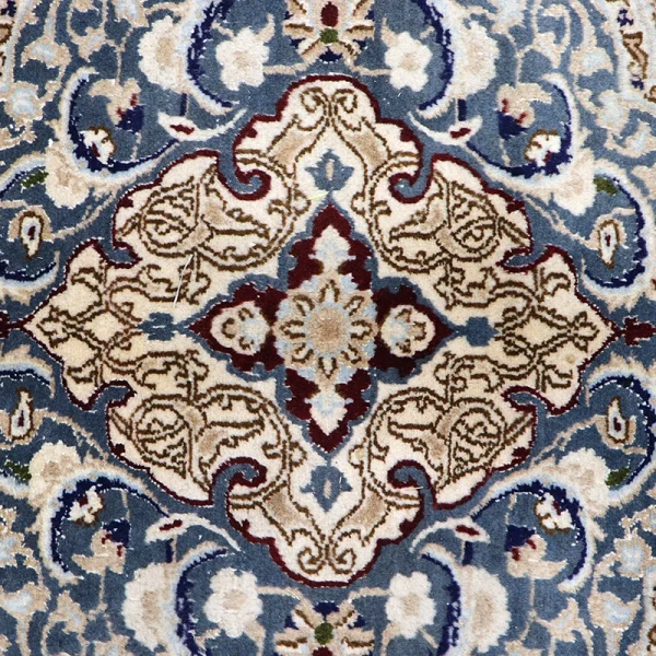 Intricate Persian-style rug pattern with a central diamond medallion in beige, burgundy, and light blue on a blue background.