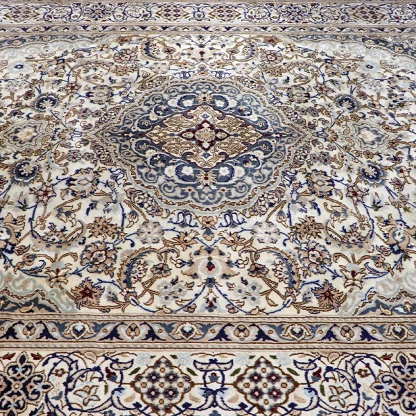 Close-up view of an ornate Persian-style rug with a blue central medallion, beige field, and delicate floral borders.