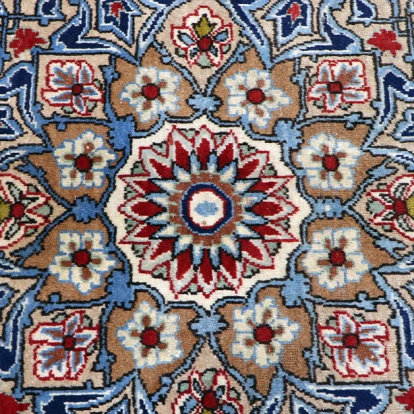 Close-up of a decorative oriental rug with a blue and red starburst central medallion on a beige background.