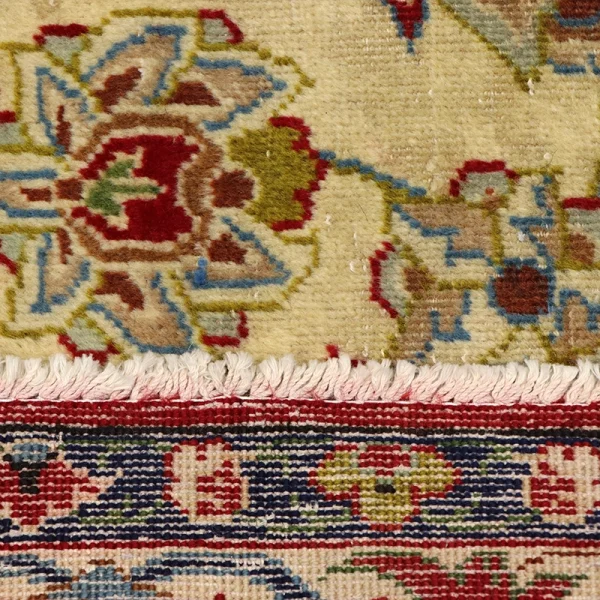 Two overlapping oriental rugs: cream and beige top rug with colorful floral motifs and a fringe at the bottom, layered over a darker patterned rug.
