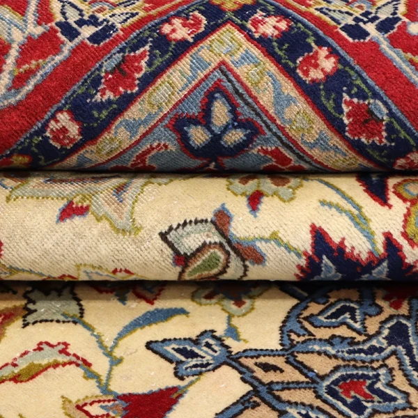 Close-up of a stack of ornate oriental rugs with red, blue, and cream floral patterns and woven texture