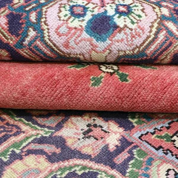 Close-up of stacked oriental rugs showing colorful geometric patterns in pink, red, blue, and green edge details.