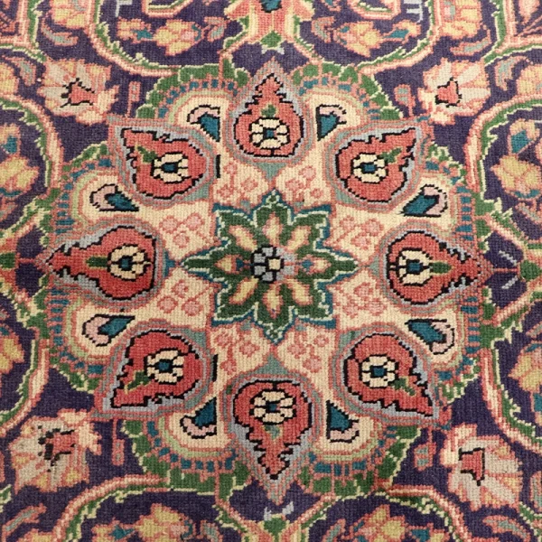 Colorful Persian rug with a central green floral medallion and pink paisley motifs on a purple border.