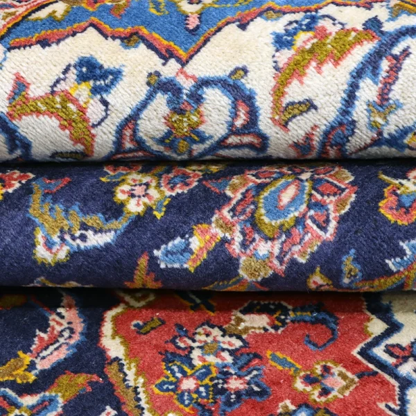 Stack of colorful patterned rugs stacked on top of each other, featuring floral motifs and red, blue, white, and cream hues