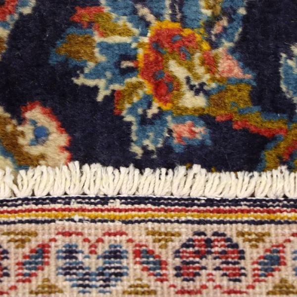 Close-up of a patterned rug with a navy blue field, multicolor floral motifs, and a cream fringe edge.